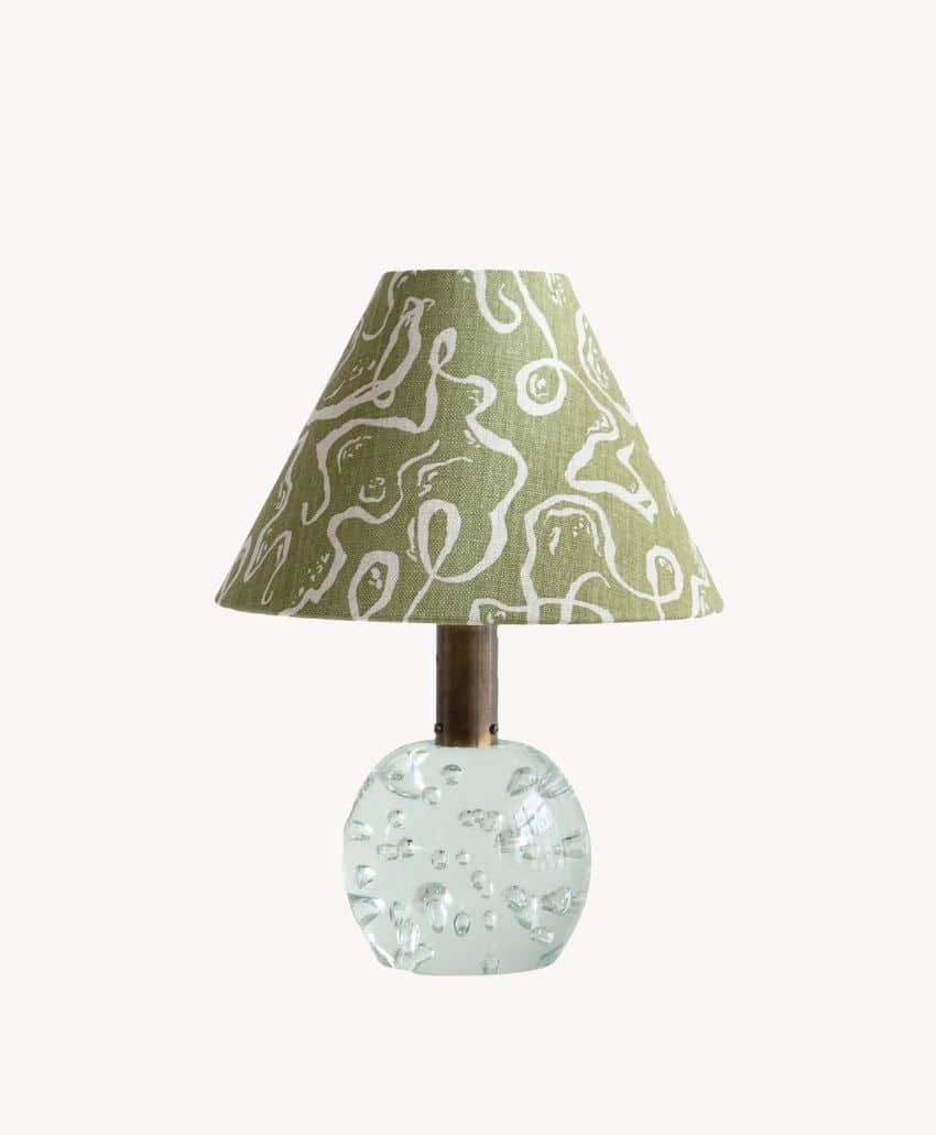 Table lamp by Cathy Nordström with a clear, textured glass base and a green conical lampshade featuring a white abstract pattern, set against a plain white background.
