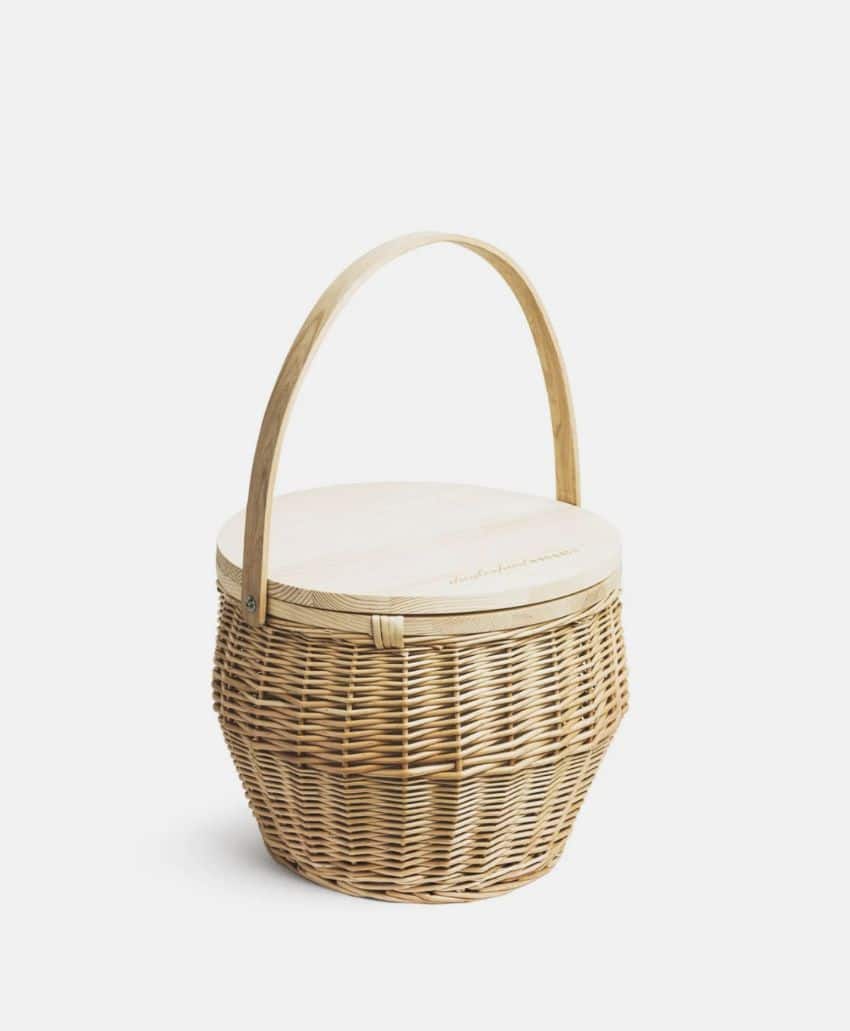 A round, woven wicker basket with a sturdy wooden handle and a flat wooden lid, set against a plain white background.