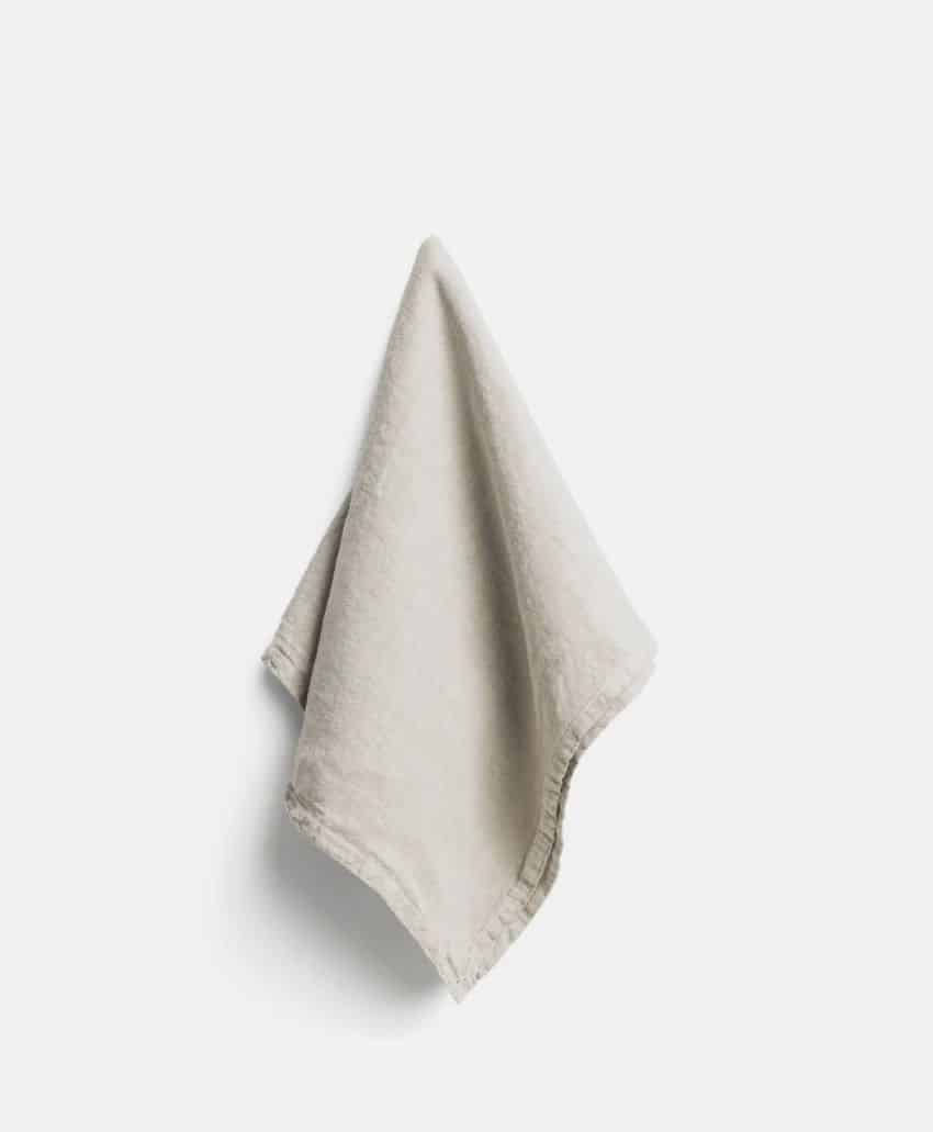 A light beige cloth or towel is hanging on a wall against a plain white background.