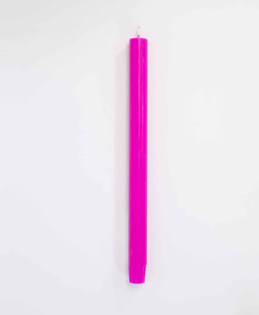 A single, unlit, bright pink taper candle is standing upright against a plain white background.