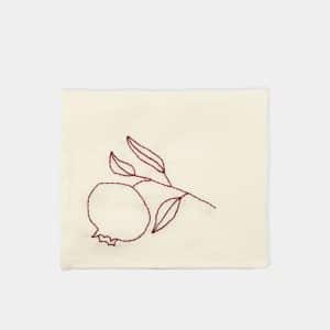 Four cream-colored rectangular placemats, each featuring a simple brown line drawing of a pomegranate with leaves in one corner, arranged in a grid on a plain light background.