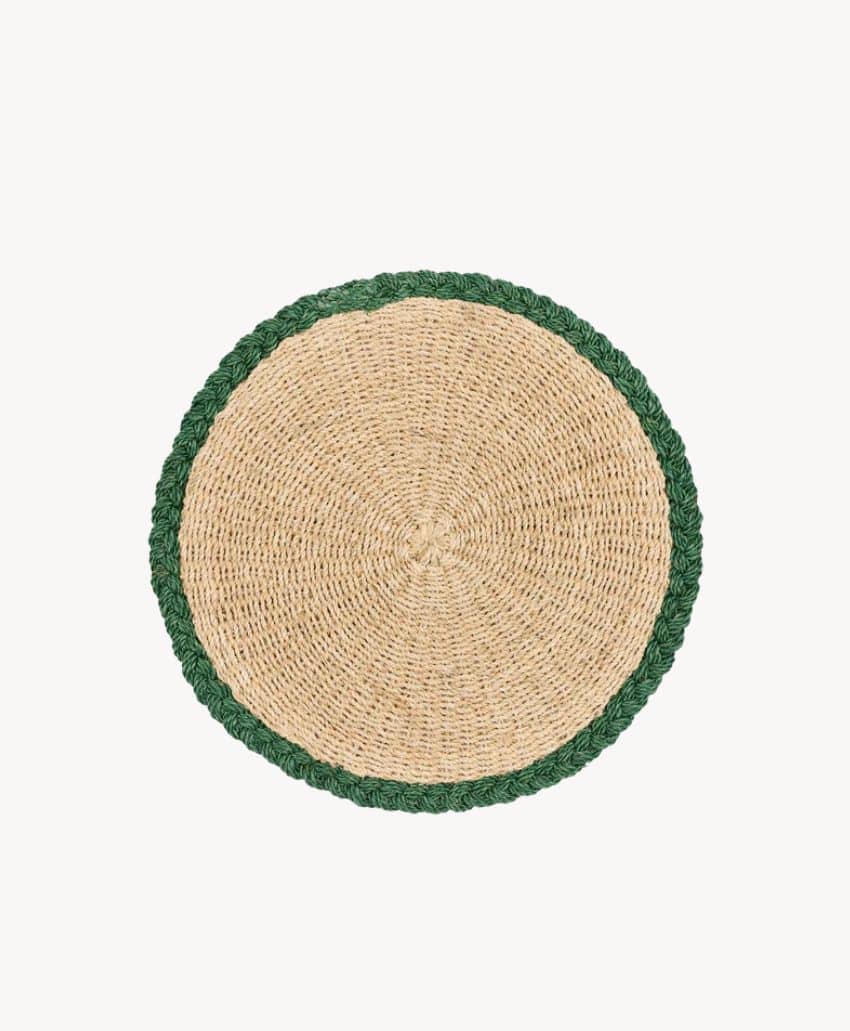 A round woven placemat made of natural fibers, featuring a tan center and a green braided border, displayed on a plain white background.