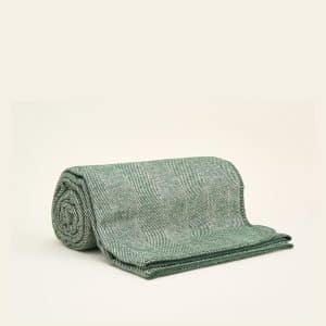 A green and white herringbone patterned blanket is neatly rolled and partially unrolled on a plain, light-colored surface.