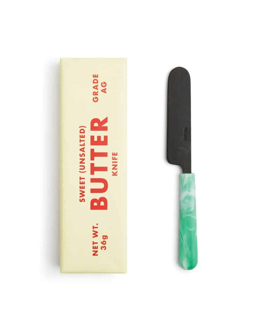 A rectangular stick of butter in cream-colored packaging labeled SWEET (UNSALTED) BUTTER beside a butter knife with a green marbled handle and a dark blade.
