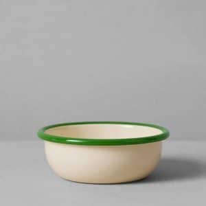 A cream-colored enamel bowl with a green rim sits on a gray surface against a gray background.