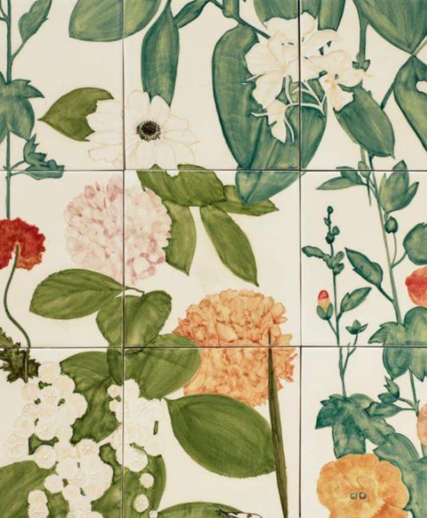 Colorful floral illustration on ceramic tiles, featuring large leaves and various flowers in white, pink, red, orange, and yellow tones, arranged against a light background.