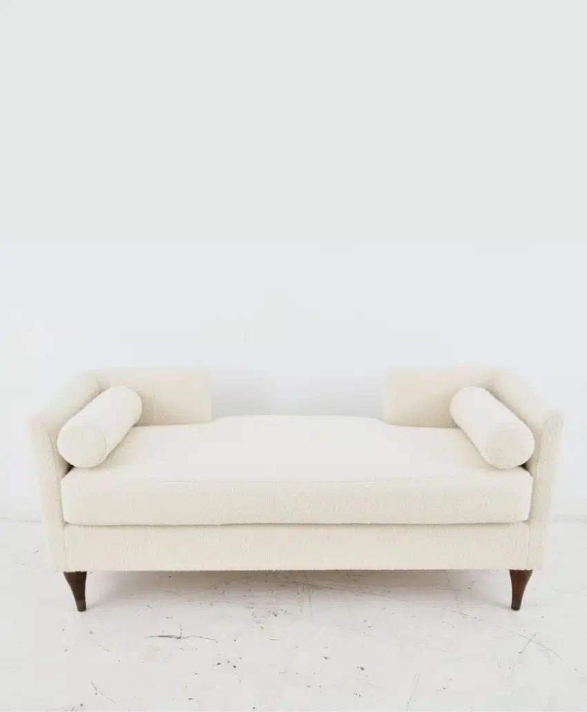 A modern cream-colored upholstered bench with two cylindrical bolster pillows at each end, wooden legs, and a minimalist design, set against a plain white background.