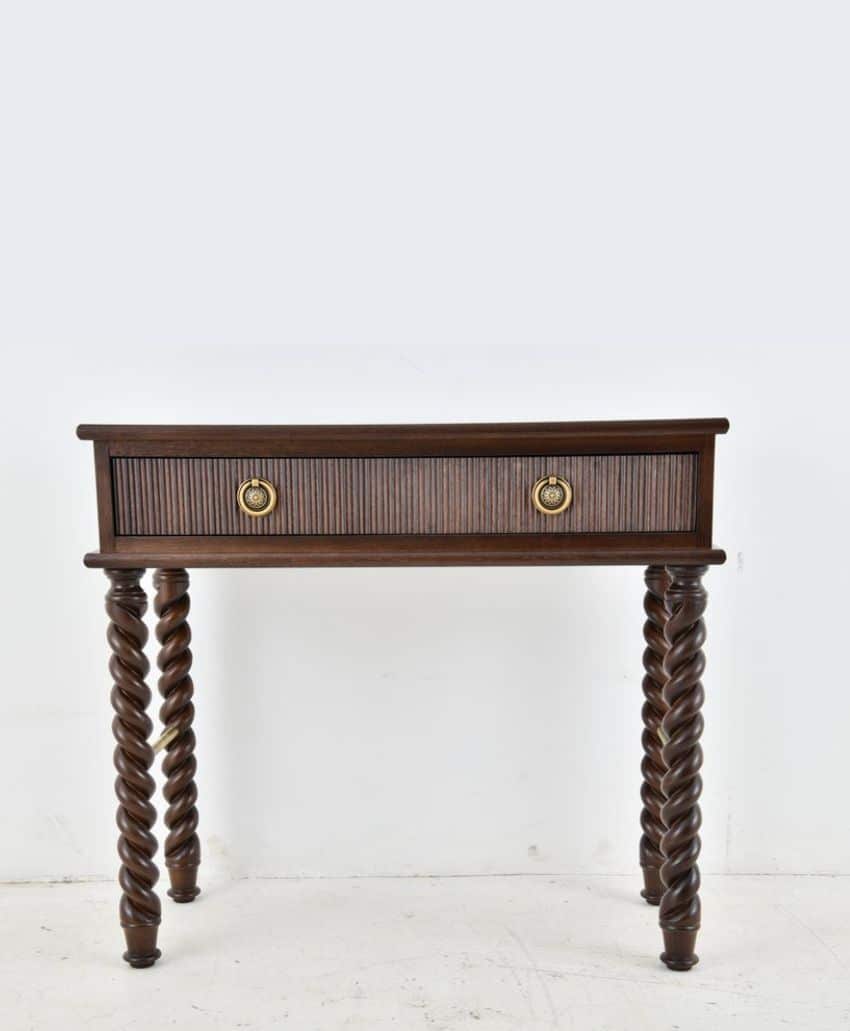 A dark wood side table with a single drawer, round gold handles, and four intricately twisted legs, set against a plain white background.