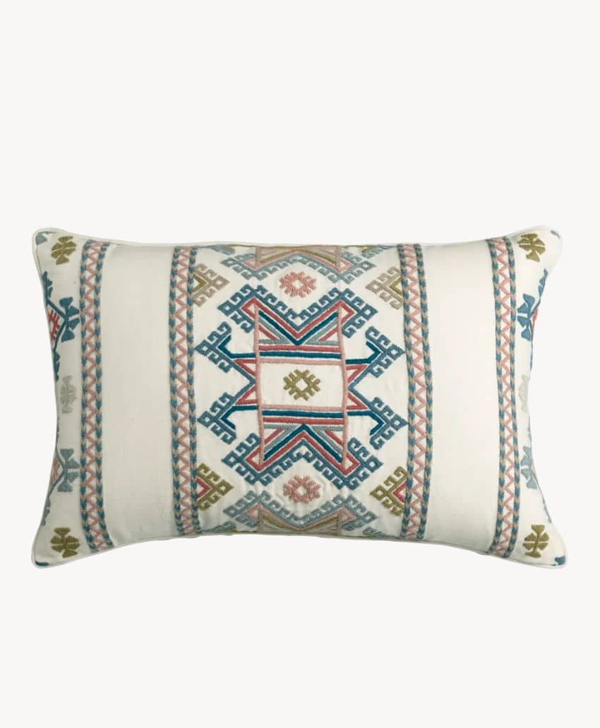 A rectangular decorative pillow featuring a central geometric pattern in blue, red, green, and gold on a white background, with matching patterned stripes along the sides.
