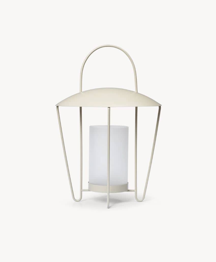 A modern, minimalist lantern with a cream-colored metal frame, arched handle, and a cylindrical frosted glass or plastic center for a light source, set against a plain white background.