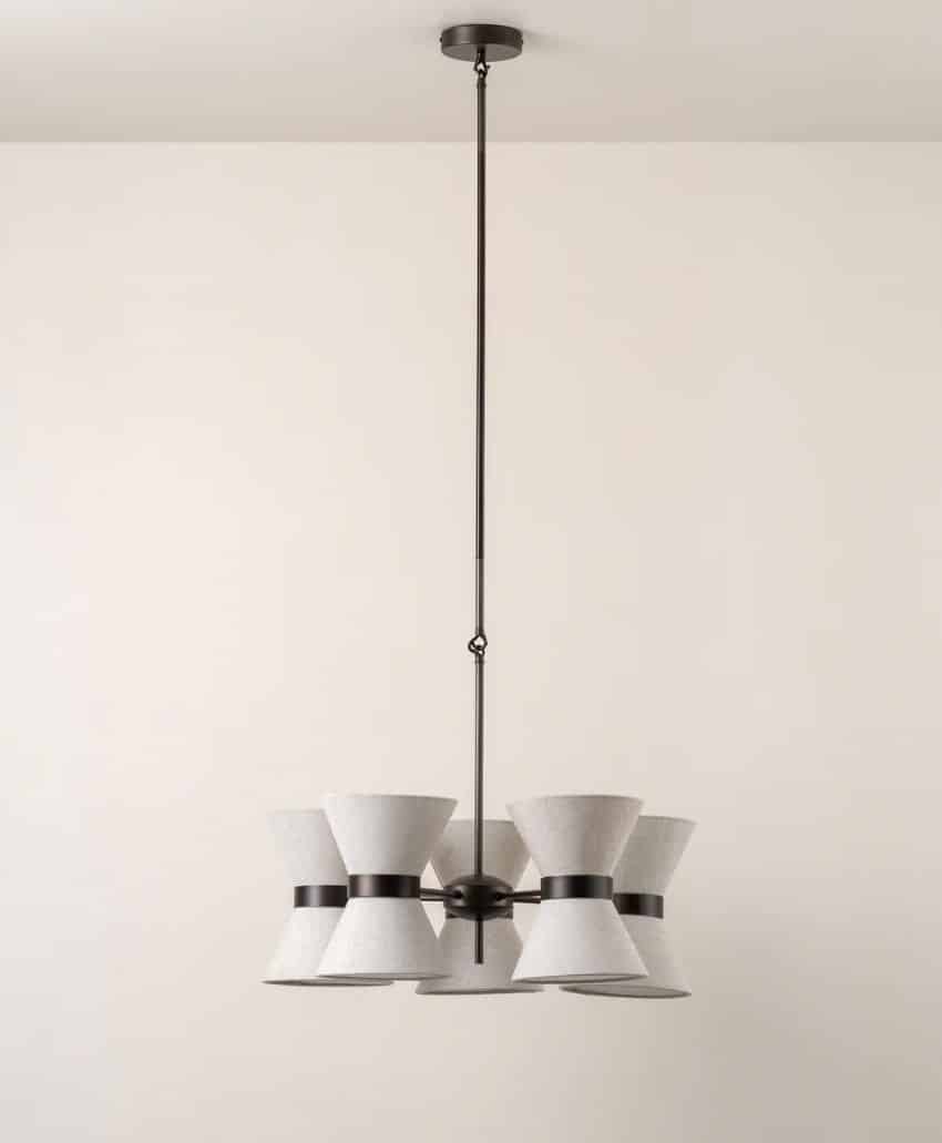 A modern pendant chandelier with six cone-shaped white lampshades arranged in a circular pattern, each with a black band, hanging from a long black rod against a plain white wall.