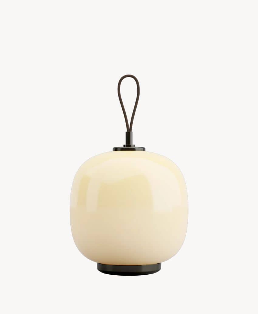 A modern, oval-shaped cream-colored table lamp with a glossy finish, black circular base, and a looped handle on top against a plain white background.