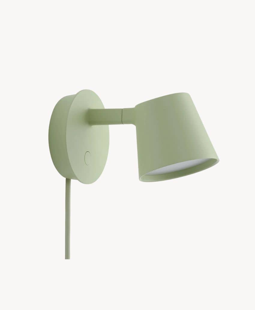 Minimalist, light green wall-mounted lamp with a round base, short arm, and angled conical shade, shown against a plain white background. A cord hangs down from the base.