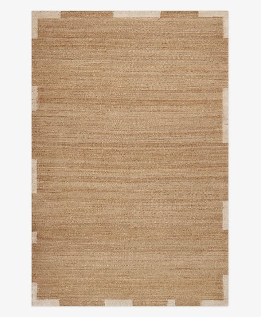 Rectangular beige area rug with a subtle striped texture and small white rectangular accents spaced along the edges, creating a simple, modern border design.