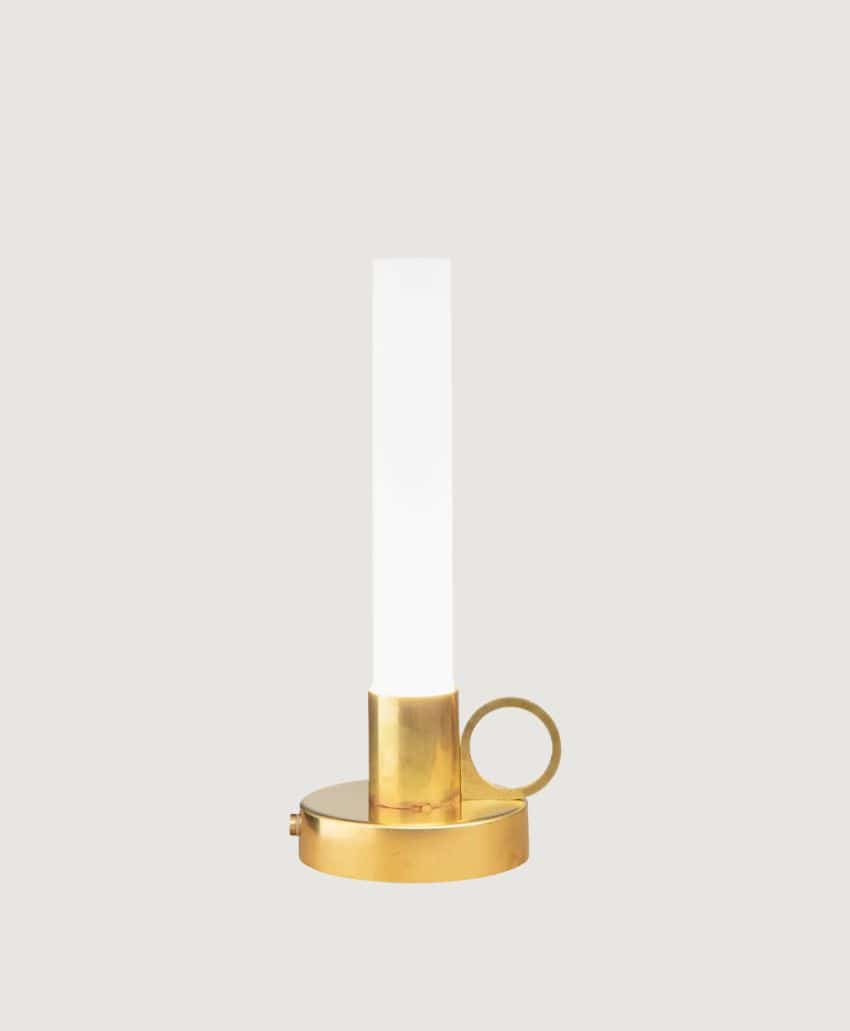 A modern candle-shaped table lamp with a cylindrical white frosted glass shade, set in a round gold base featuring a small handle and a side switch, displayed against a plain light background.