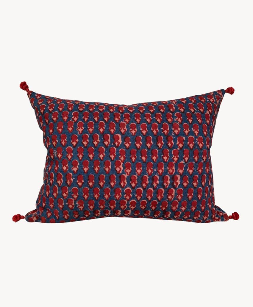 A rectangular pillow with a dark blue background and a repeating red floral pattern, featuring red tassels on each corner.
