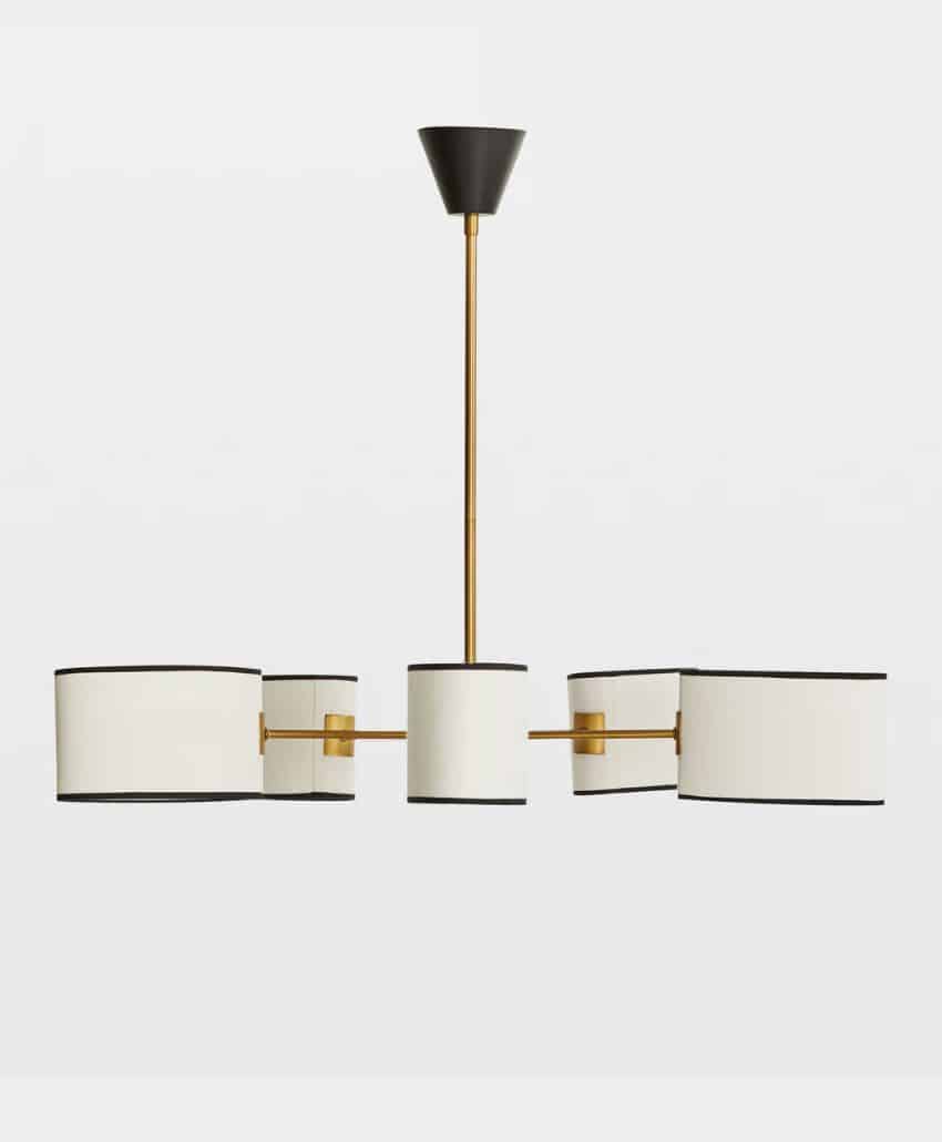 A modern chandelier with five cylindrical white lampshades, black edges, and gold metal arms, suspended from a gold rod with a black ceiling mount against a plain white background.