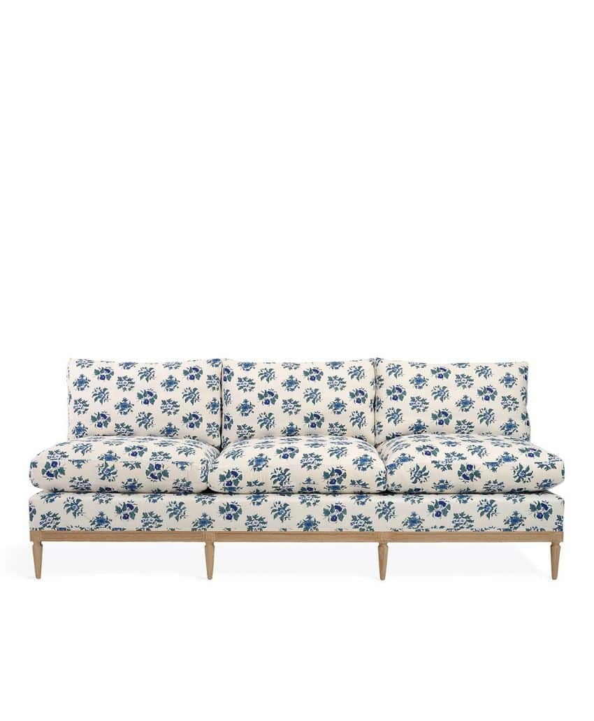 A long, three-cushion sofa with light wooden legs, upholstered in white fabric featuring a blue floral pattern.