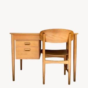 A wooden desk with two drawers and a matching wooden chair are placed together against a plain white background.