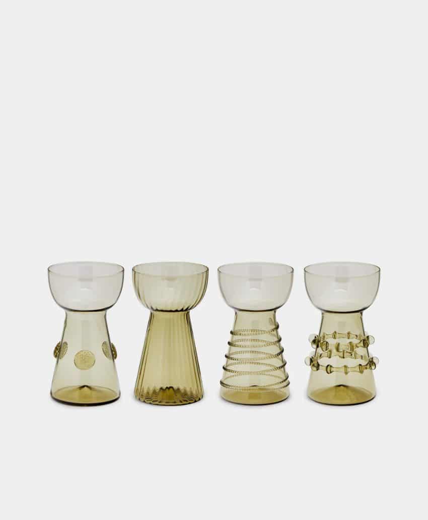 Four uniquely designed, transparent amber-colored glass goblets are lined up side by side on a plain light background. Each goblet has a distinct textured pattern on its base.