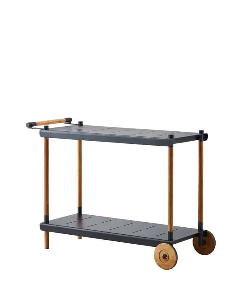 A modern serving cart with a rectangular black top and bottom shelf, wooden legs, two large wooden wheels on one side, and a wooden handlebar.