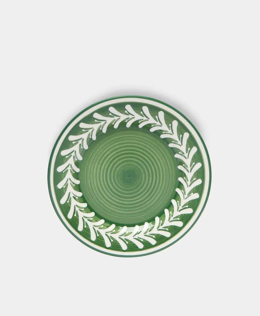 A round green ceramic plate with a white leafy vine pattern circling the rim, set against a plain light background.