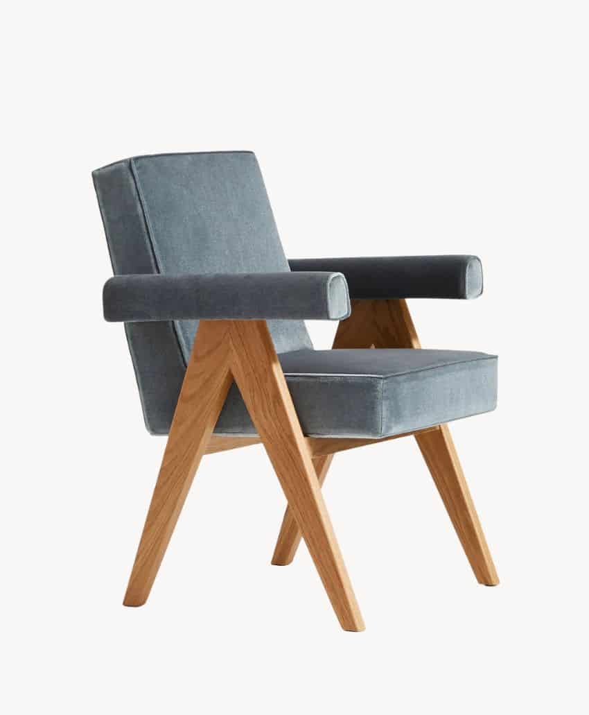 A modern armchair with a blue upholstered seat, backrest, and armrests, featuring angled wooden legs and frame in a light wood finish, set against a plain white background.