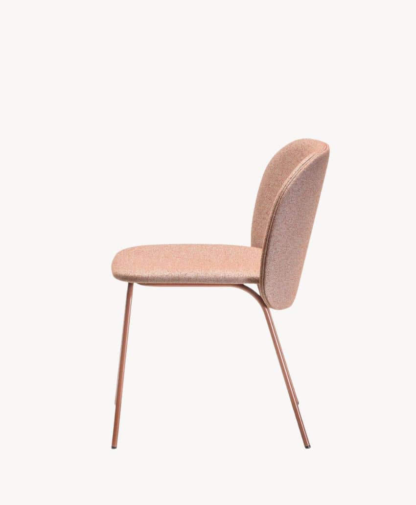 Side view of a modern upholstered chair with a curved backrest and slender metal legs, all in a light, muted pink color, set against a plain white background.