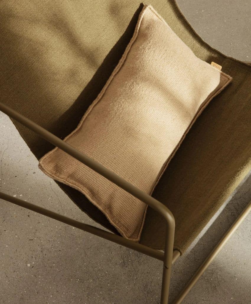 A beige rectangular cushion rests on an olive-green sling chair with a metal frame, set on a speckled gray concrete floor in warm, natural light.