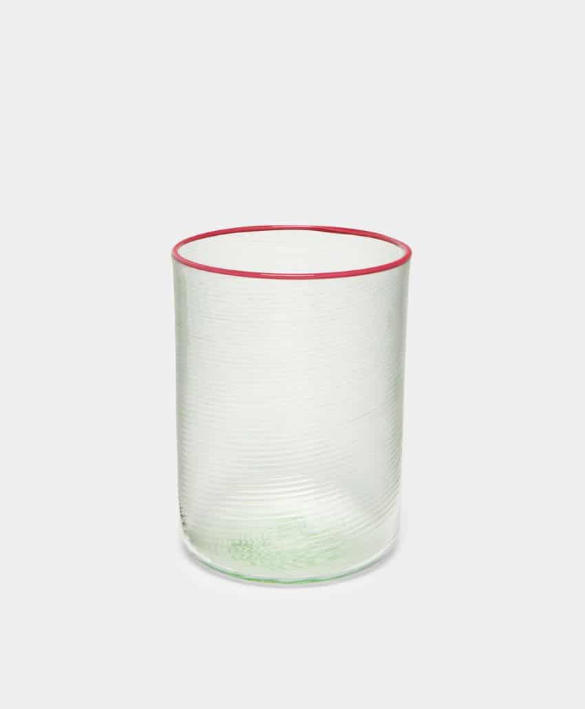 A clear glass tumbler with a subtle textured pattern and a thin red rim, placed against a plain light gray background.