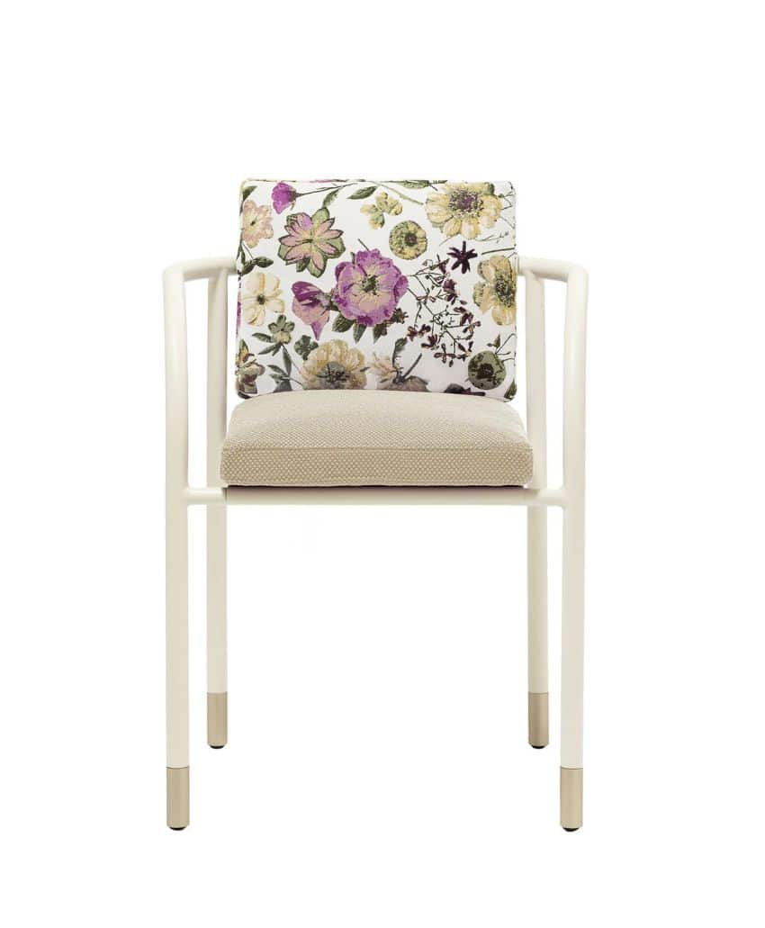 A white chair with straight arms, a beige seat cushion, and a back cushion featuring a colorful floral pattern with green, purple, and yellow flowers. The chair legs have metallic caps at the bottom.