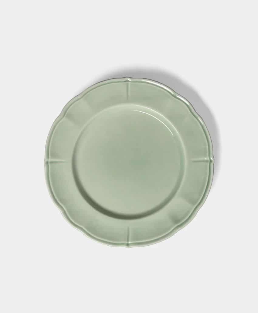 A light green ceramic plate with a scalloped edge and subtle ridges, shown from above on a plain light background.