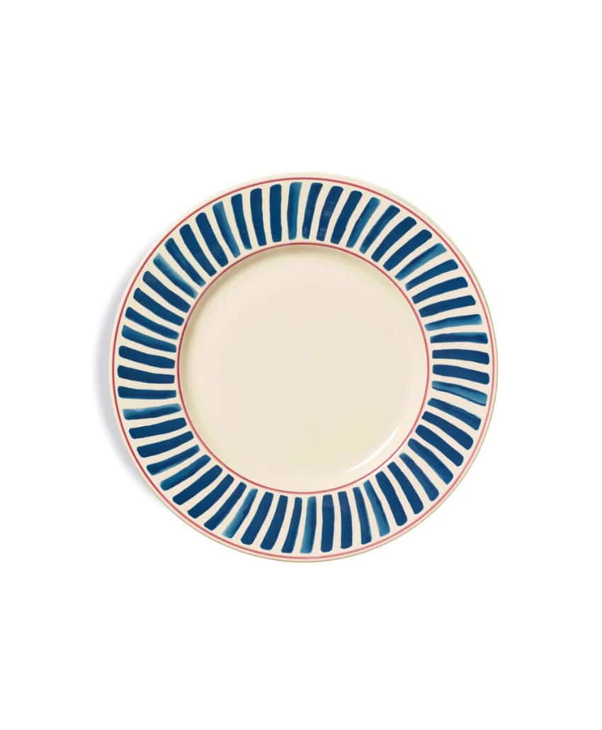 A round ceramic plate with a cream-colored center and a border of blue vertical brushstroke patterns, outlined by a thin red rim.