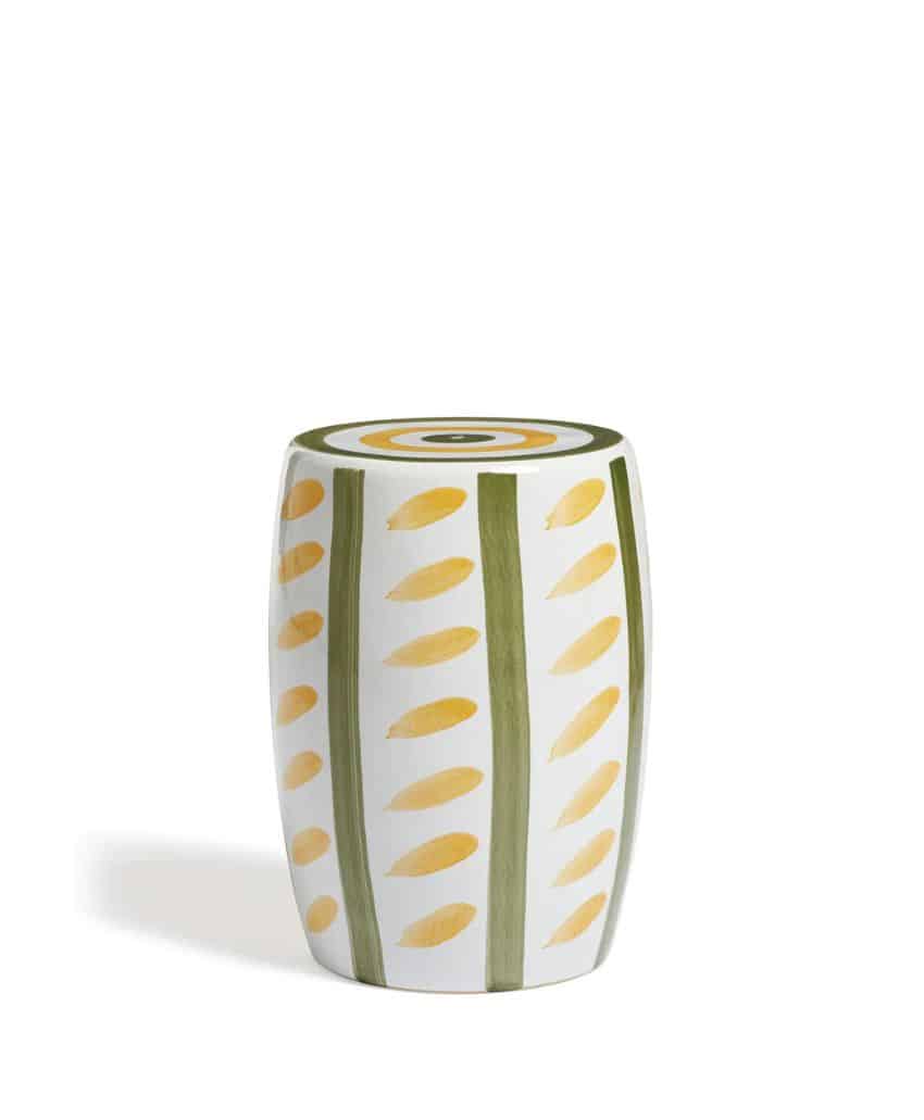 A cylindrical ceramic stool with yellow leaf patterns and vertical green stripes, topped with concentric circles in yellow, green, and white, set against a plain white background.