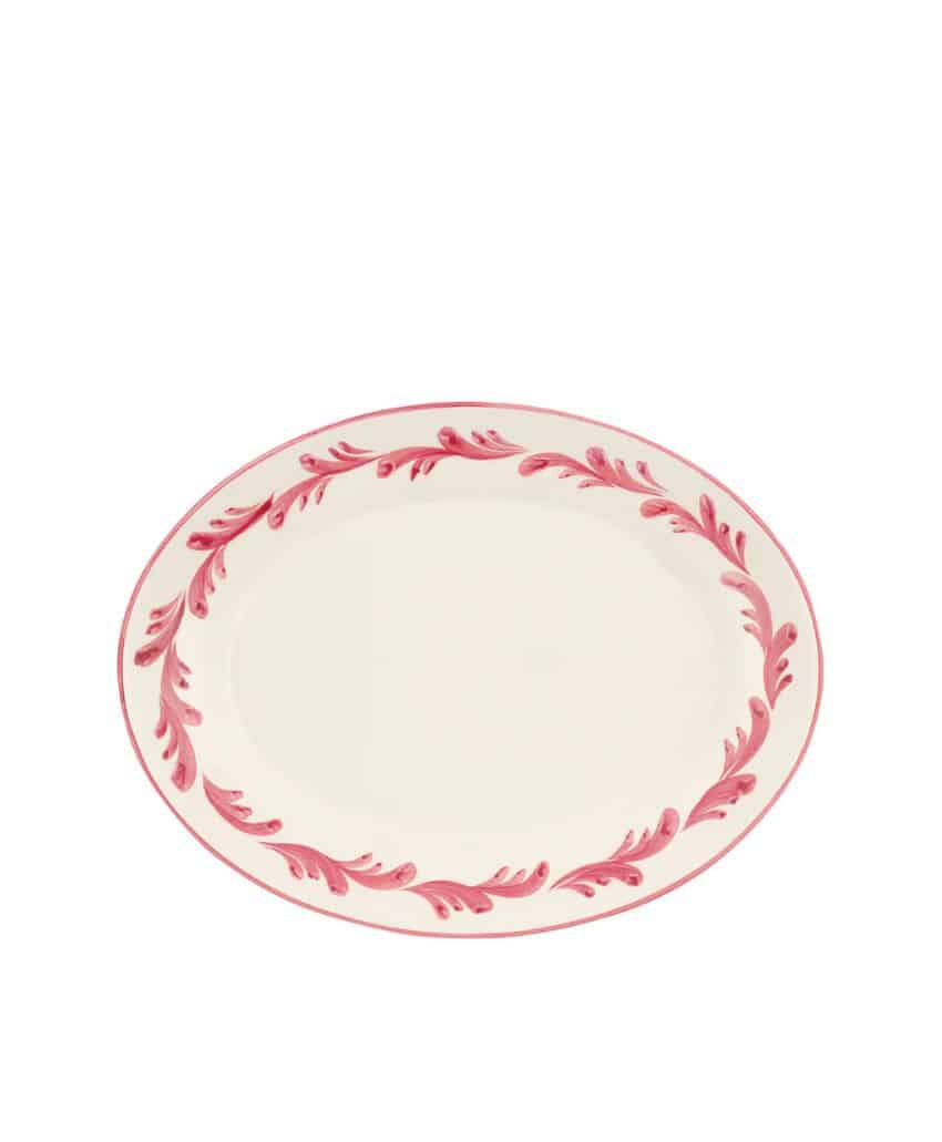 An oval-shaped, cream-colored plate with a pink floral or leaf pattern around the rim.