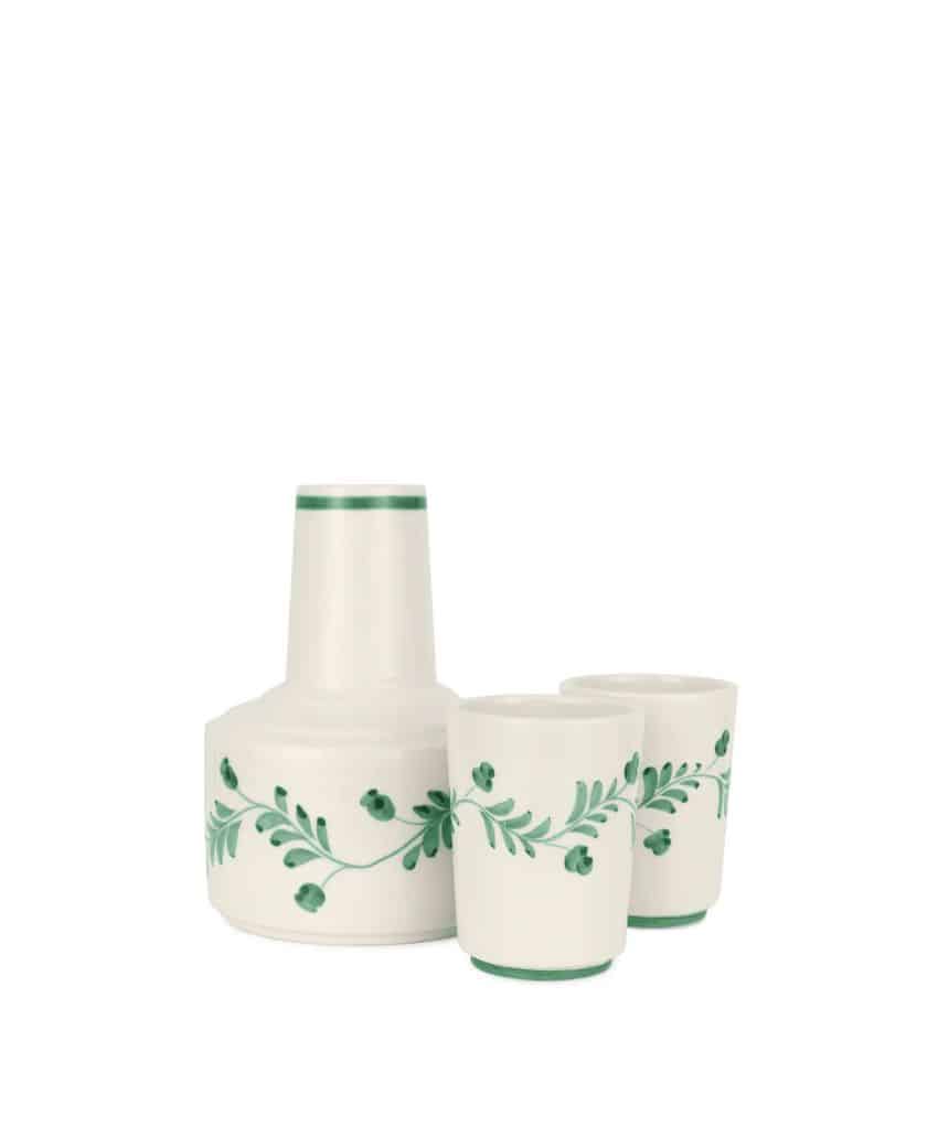 A ceramic carafe with two matching cups, all white with green floral and leaf patterns and a green rim near the top, displayed on a plain white background.
