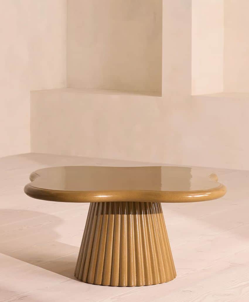 A round, glossy wooden coffee table with a fluted, cone-shaped base sits on a light-colored floor against a neutral, minimalistic background.