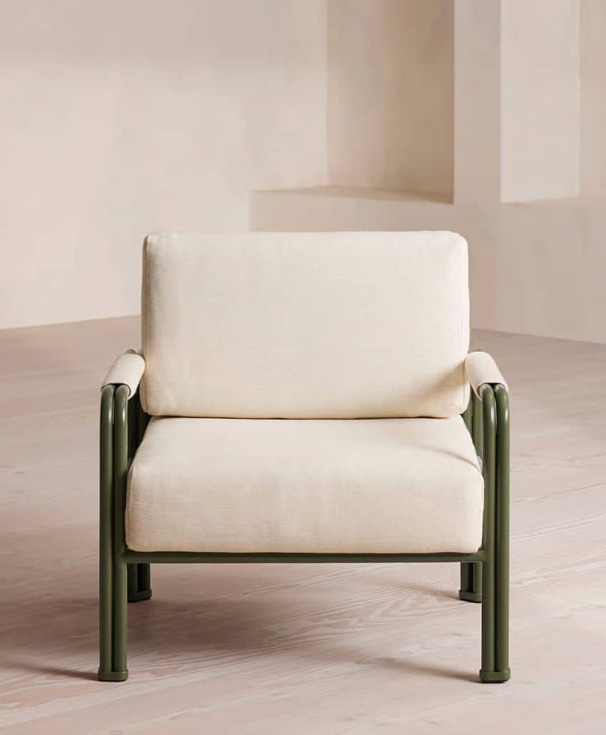 A modern armchair with a matte dark green metal frame and off-white cushioned seat and backrest, placed on a light wooden floor against a neutral beige background.