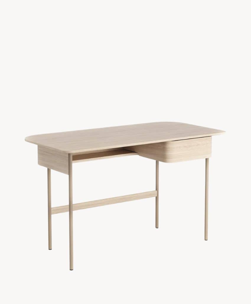 A minimalist wooden desk with a light finish, featuring four slender legs and a single drawer on the right side. The desk has rounded corners and a clean, modern design.
