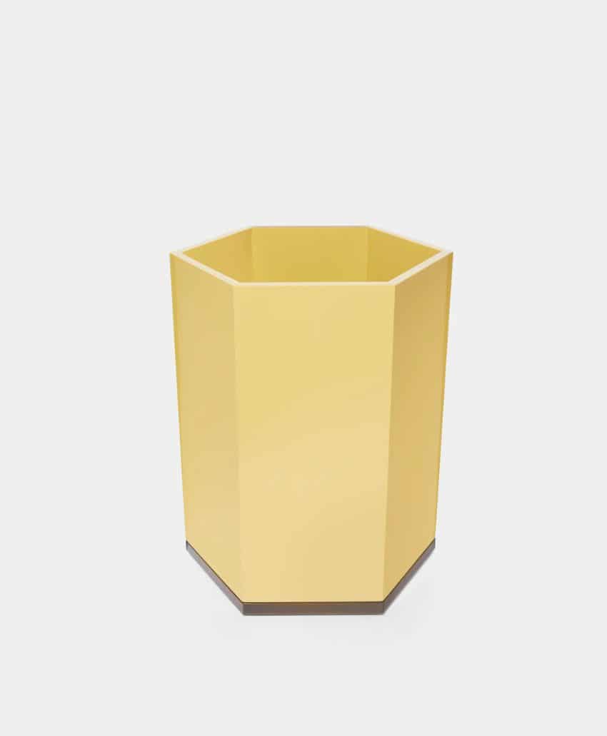 A yellow, hexagonal-shaped container or wastebasket with a matte finish, placed on a plain light gray background.