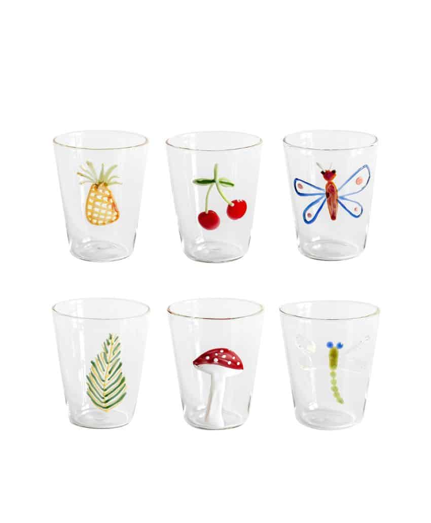 Six clear glasses each featuring a different colorful design: a pineapple, cherries, a butterfly, a green leaf, a red mushroom with white spots, and a dragonfly.