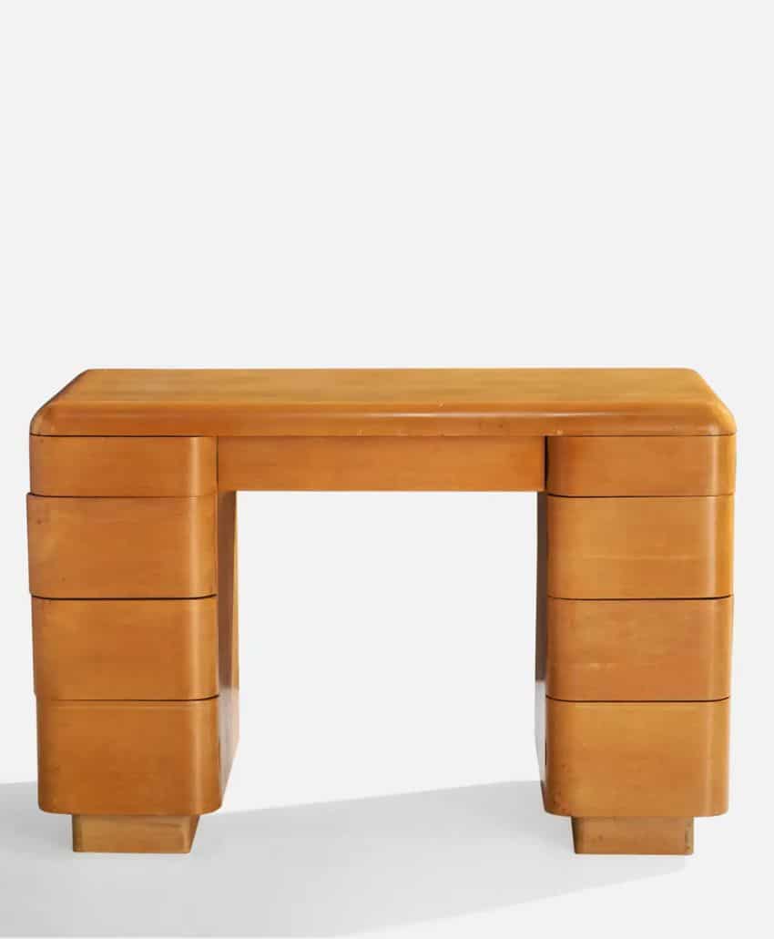 A small, vintage wooden desk with a light brown finish, rounded corners, and three drawers on each side. The design is minimalist and symmetrical, with sturdy legs and a smooth surface.