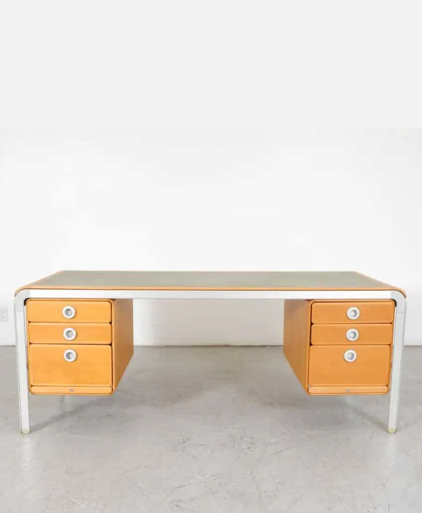 A mid-century modern desk with a green top, white frame, and two sets of four wooden drawers on each side, each drawer featuring a round white handle. The desk sits on a light gray floor against a white wall.