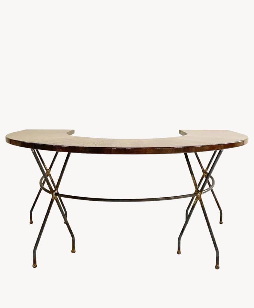 A semi-circular wooden table with a flat back and metal legs that cross in an X shape, connected by a curved support bar. The design is minimalist and industrial.