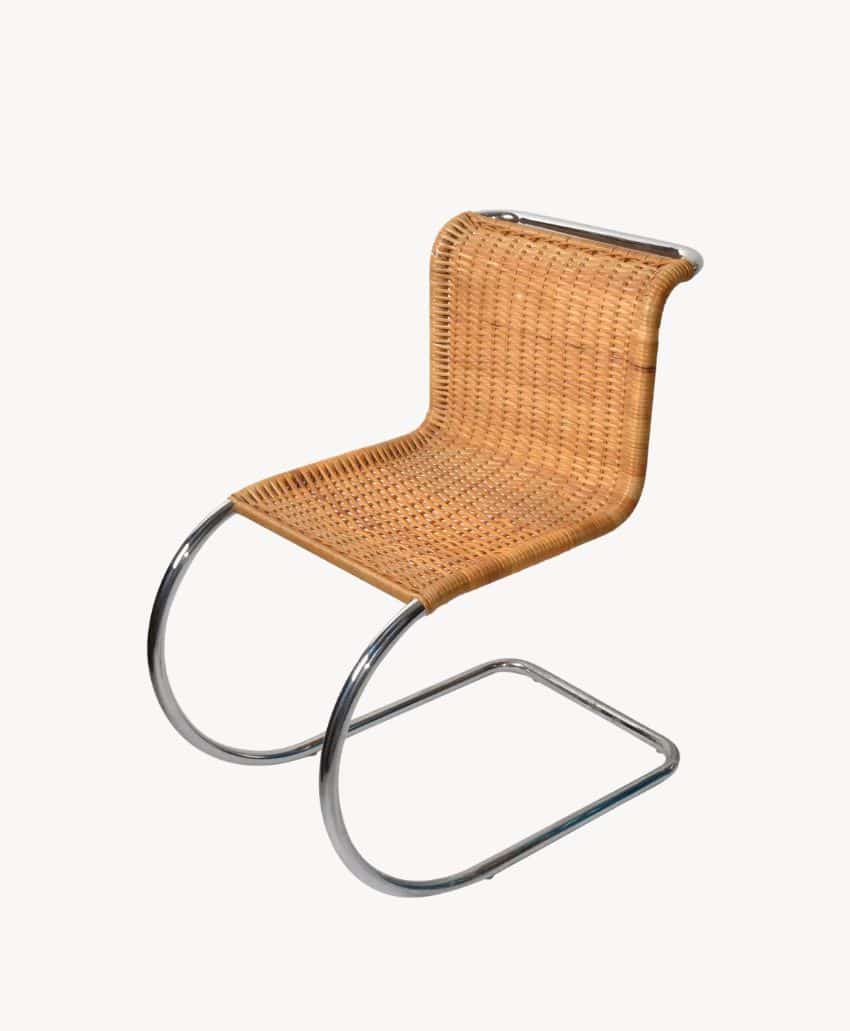 A modern chair with a tubular chrome frame and a woven cane seat and backrest, featuring a cantilevered design with no back legs, set against a plain light background.