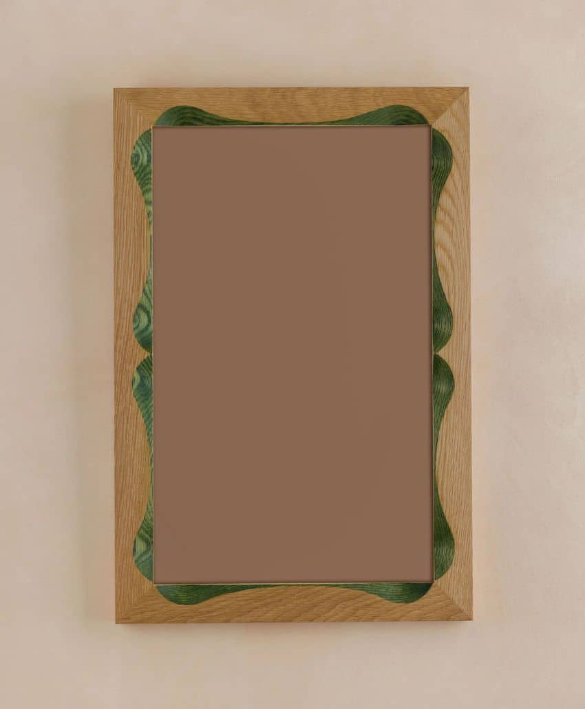 A rectangular wall mirror with a light wood frame featuring wavy green accents along the inner edge, hanging on a beige wall.