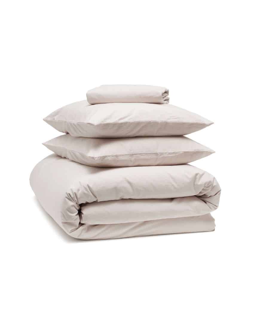 A neatly folded set of light beige bedding, including a duvet cover, two pillowcases, and a fitted sheet, stacked on top of each other against a white background.