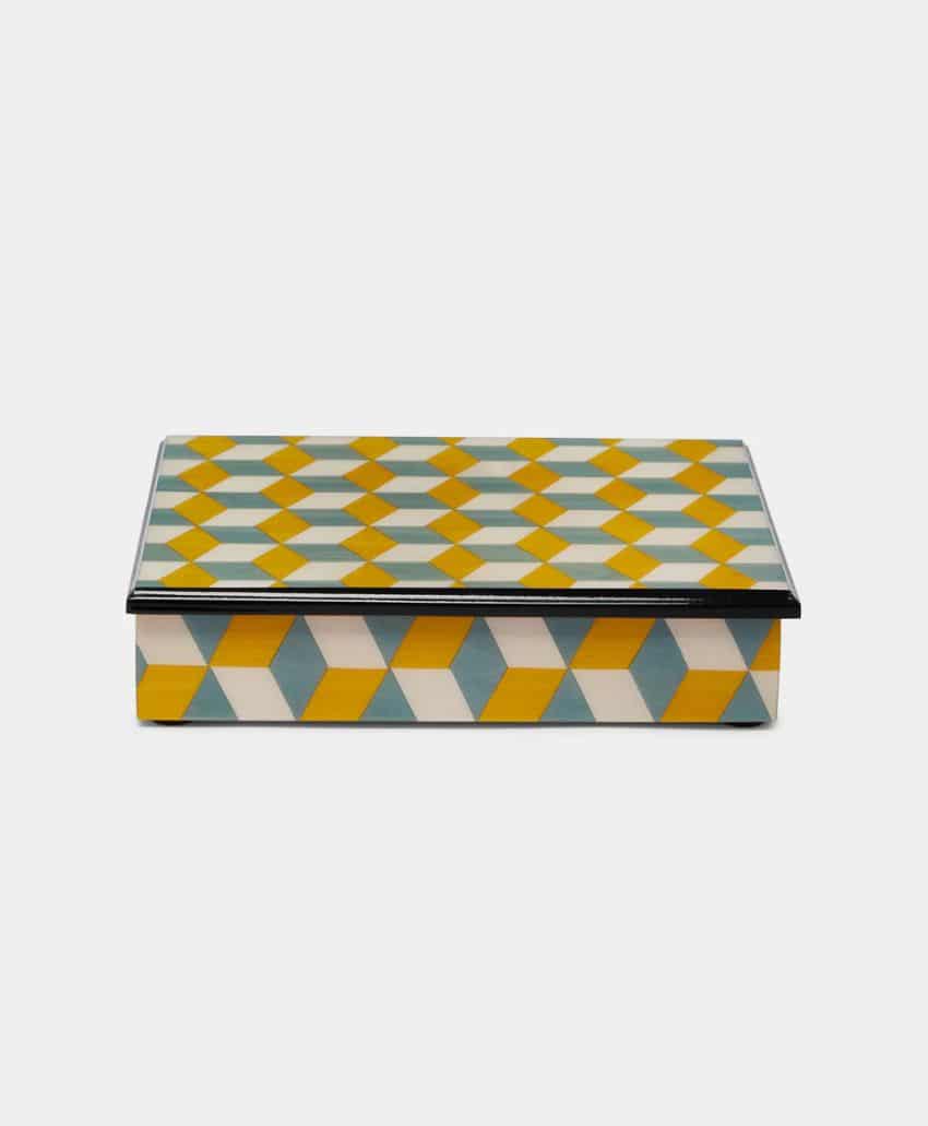 A rectangular box with a geometric pattern of yellow, blue, and white cubes on the lid and sides, set against a plain white background.