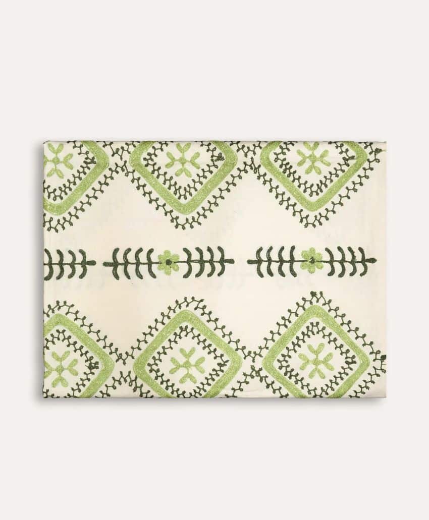 A folded cream-colored fabric featuring a pattern of green geometric shapes and floral designs arranged in rows.