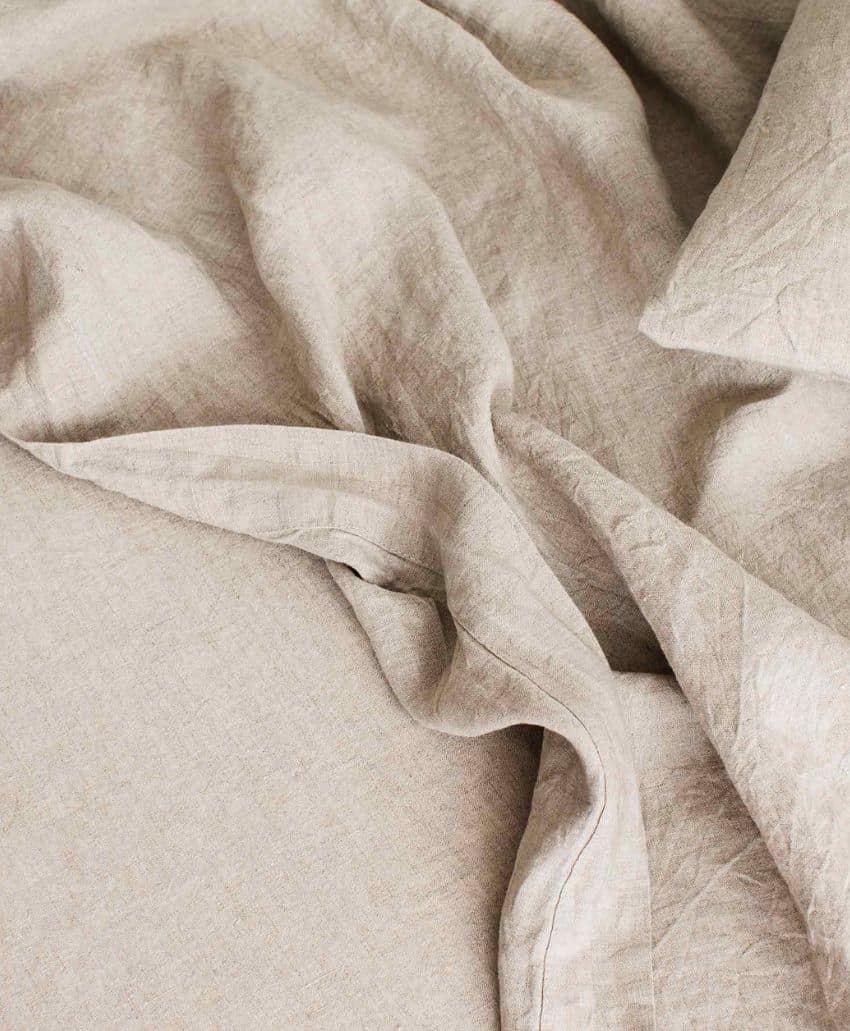 Close-up of beige, wrinkled linen fabric with soft folds and creases, creating a textured and cozy appearance.